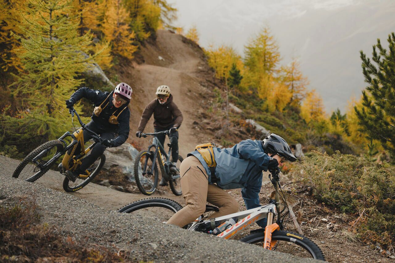 Drei Mountainbiker auf einem Feldweg inmitten von Herbstlaub.