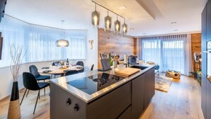 A modern kitchen with a central island, pendant lighting, and a dining area with chairs and a table.