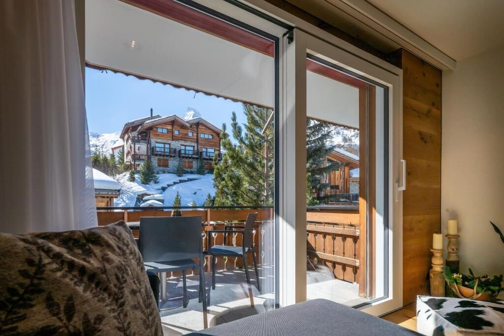 Una stanza con un letto, una finestra e vista su un edificio con facciata in legno e terreno innevato.
