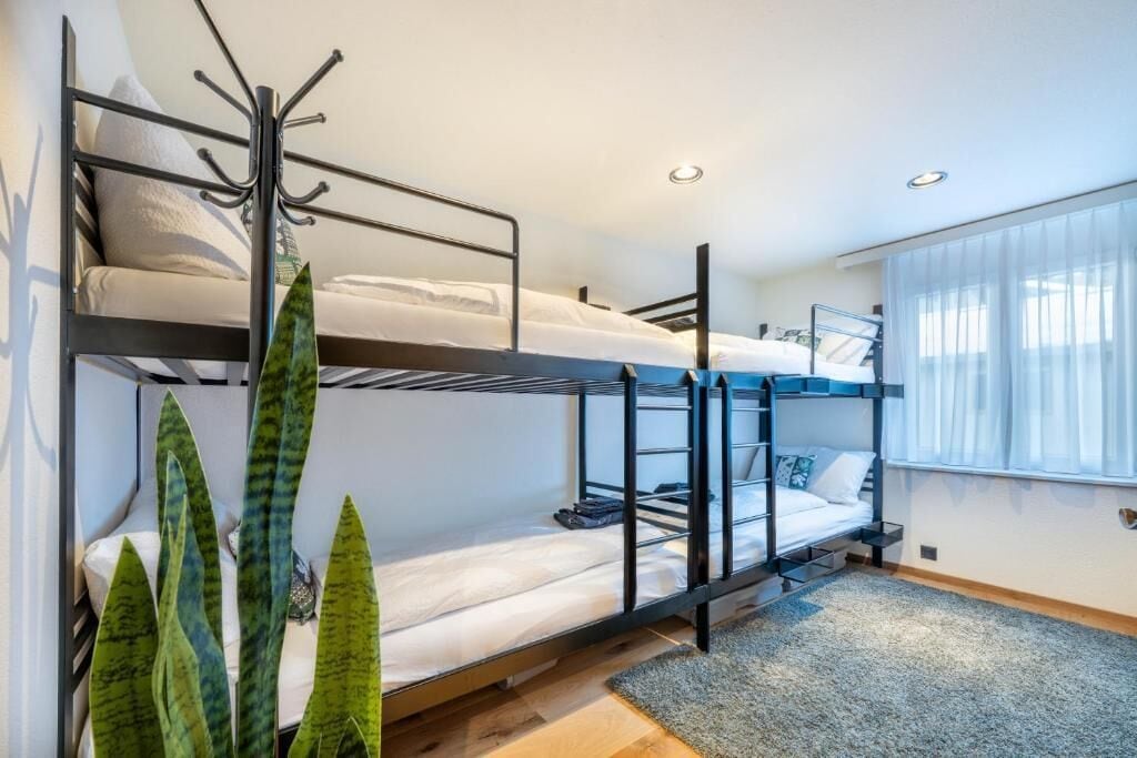 Habitació amb llits superposats, un penjador, una finestra amb cortines i una planta.