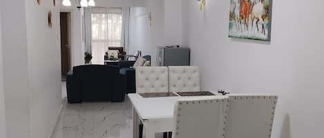 A modern living room with a dining area, a kitchen in the background, and a painting on the wall.