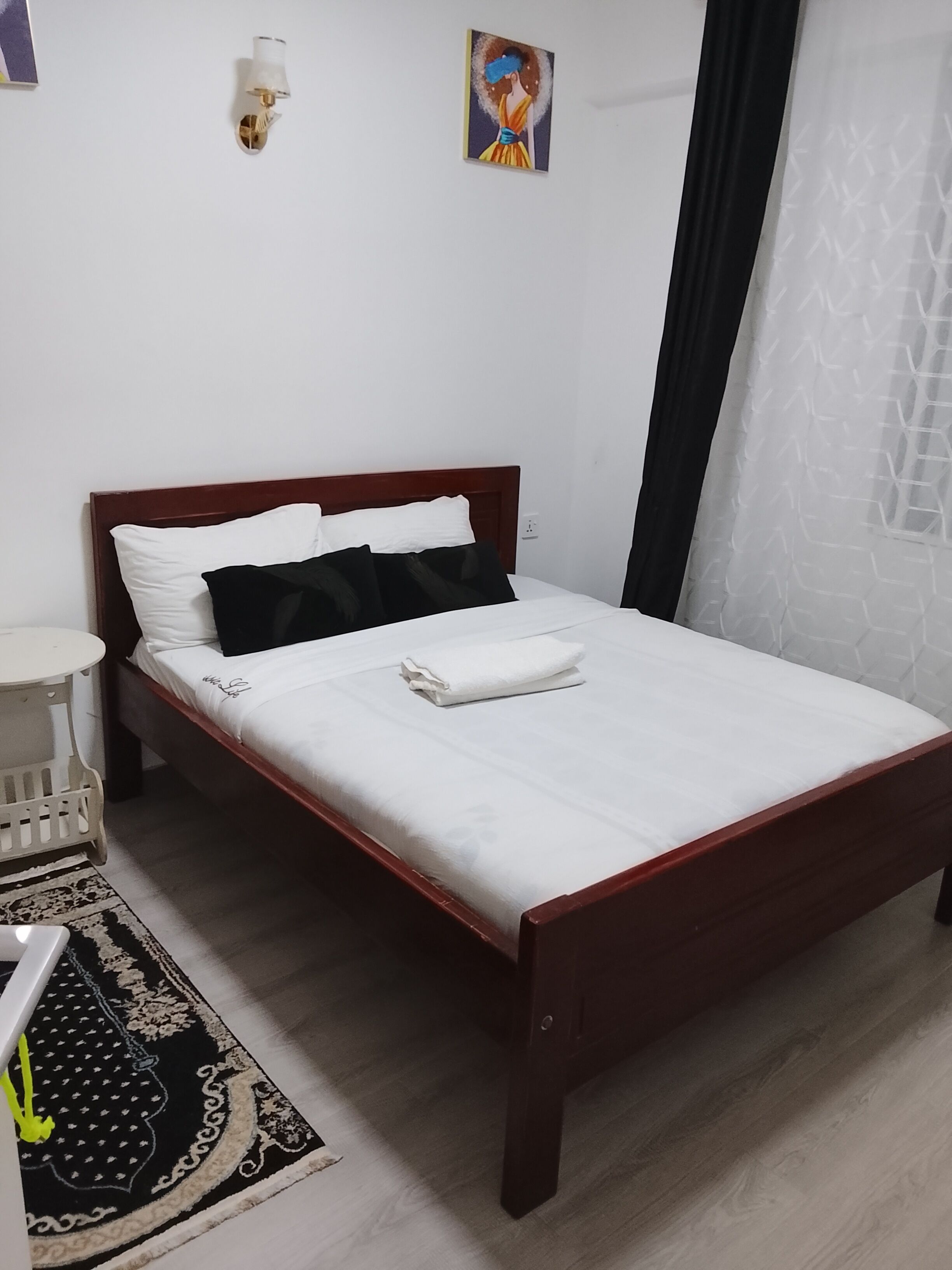 Ein ordentlich bezogenes Bett mit weißen Leinentüchern und einem gefalteten Handtuch, ein Nachttisch mit einer Lampe, ein kleiner weißer Stuhl und ein gemusterter Teppich auf dem Boden.