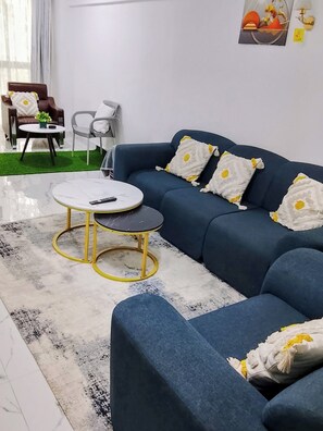 A modern living room with a blue sofa, two round tables, a coffee table, and a small rug. - Two bedroom apartment in Kilimani (Nairobi)