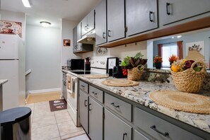A kitchen with grey cabinets, a white refrigerator, a black coffee machine, and woven baskets on the counter.