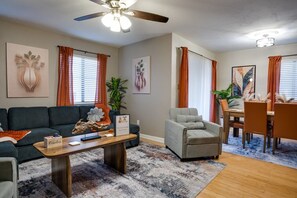 A living room with a sofa, armchair, coffee table, and a dining area with chairs and a table.