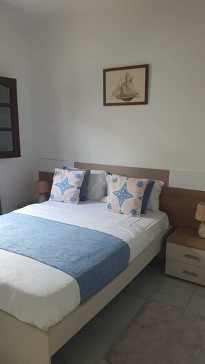 A bedroom with a bed, pillows, a nightstand, a lamp, and a framed picture on the wall.
