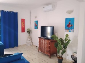 Ein Wohnzimmer mit Fernseher auf einer Holzkommode, einem blauen Sofa, einer Topfpflanze und Bildern an den Wänden.