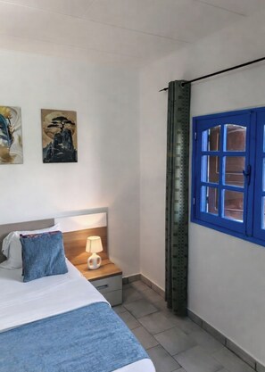 Ein Hotelzimmer mit einem Bett, einem Nachttisch mit Lampe, einer blauen Tür und zwei Bildern an der Wand.