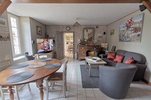 A living room with a wooden dining table, grey sofa, and a television. - Family home with a garden, 3 bedrooms, near Puy du Fou (Saint-Amand-sur-Sèvre)