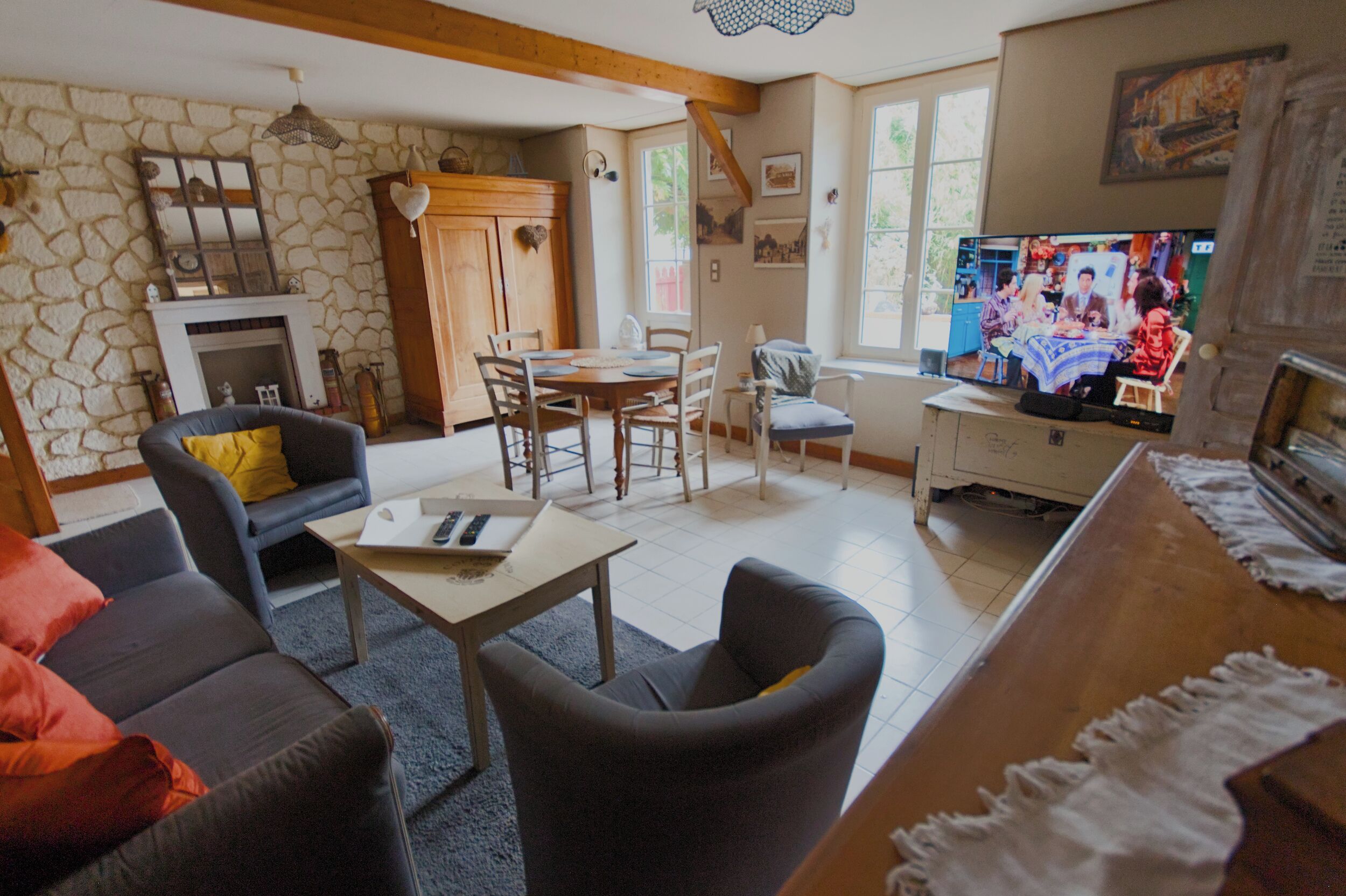 A cozy living room with a stone wall, a fireplace, a dining area with a table and chairs, and a television.