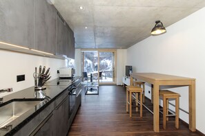 A modern kitchen with a large island, stainless steel appliances, and a view of a snowy landscape through the glass door. - Hoodoo panorama apartment ,House Mojo Zermatt (Zermatt)