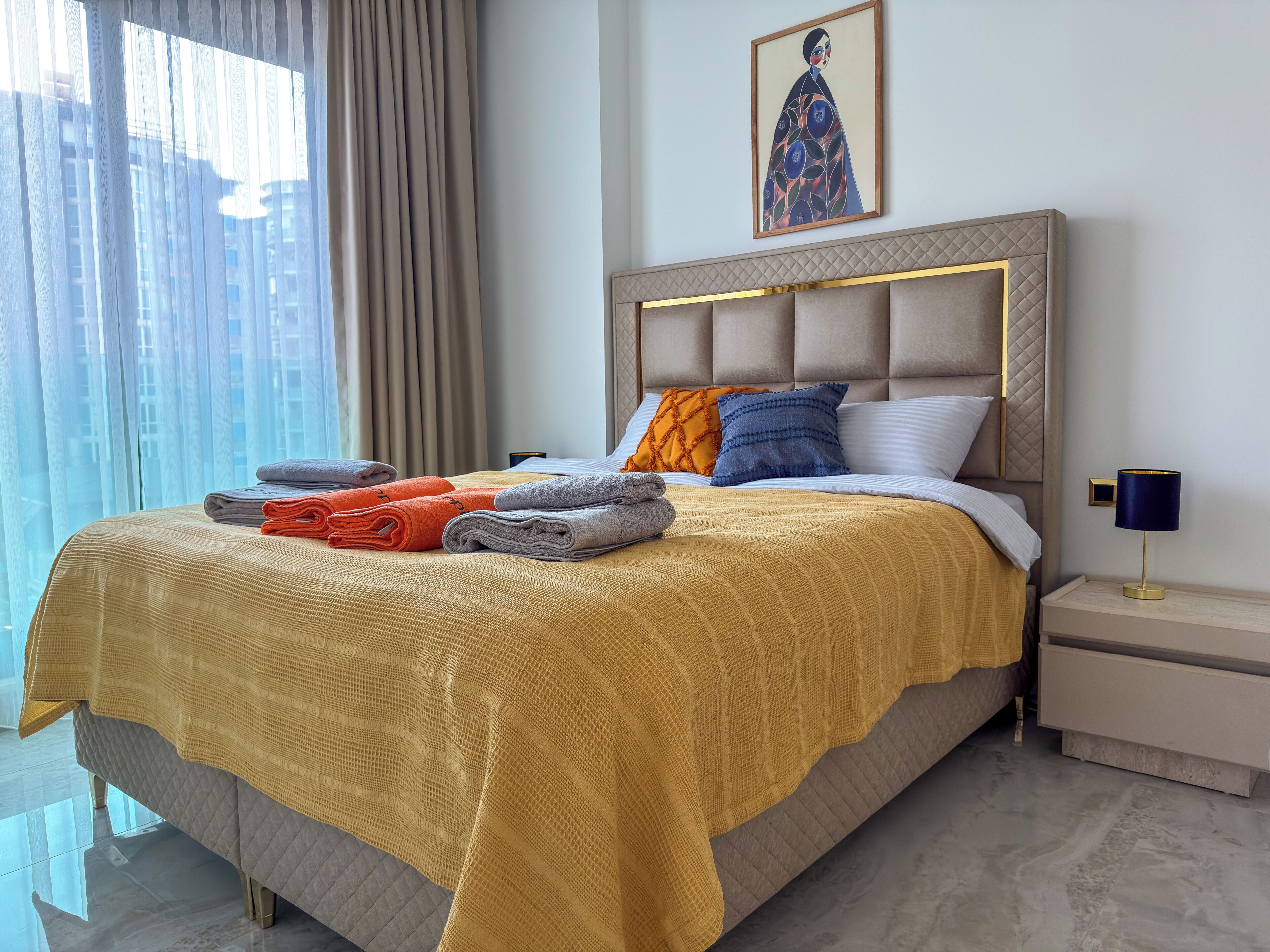 A hotel room with a bed, a nightstand, a lamp, a painting, and a window with curtains.