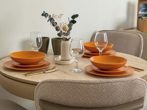 Ein runder Esstisch mit orangefarbenen Tellern, klaren Gläsern und einer Vase mit Trockenblumen.