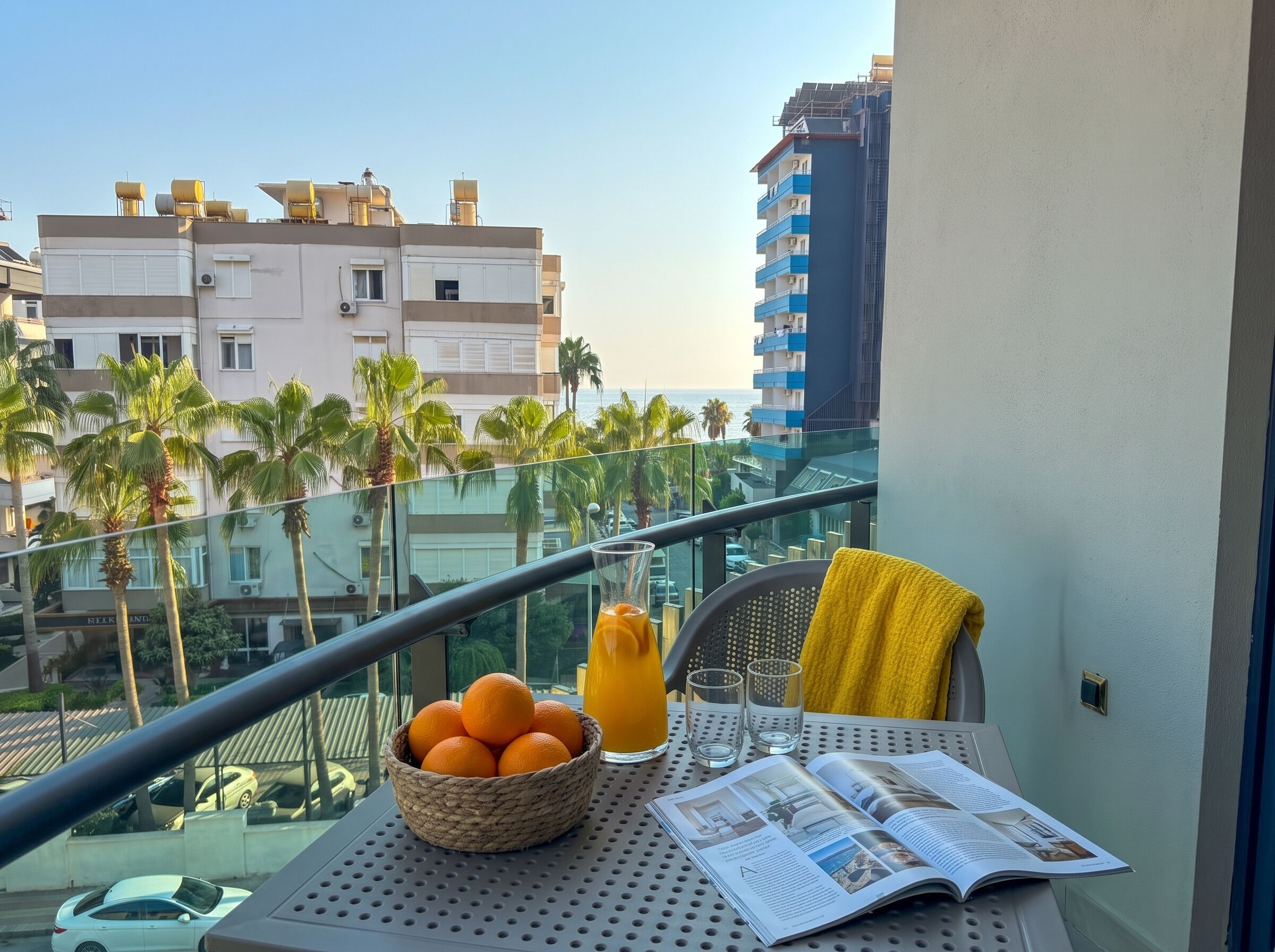 A balcony with a table, a basket of oranges, a glass of orange juice, and a magazine.