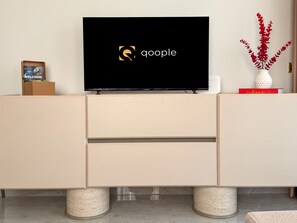 Ein Flachbildfernseher auf einer Holzkassette, auf dem ein Logo zu sehen ist, eine Kartonbox und eine dekorative Vase mit roten Blumen.