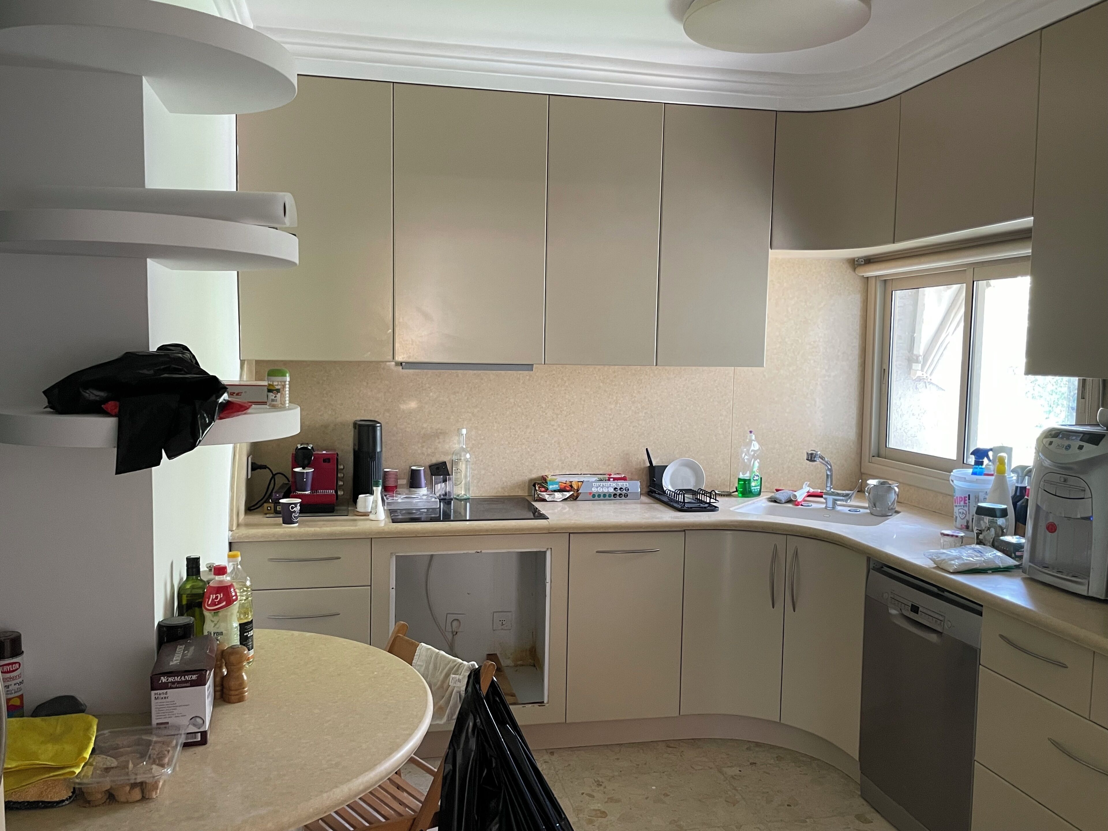 A kitchen with a round dining table, cabinets, a window, and various kitchen appliances.