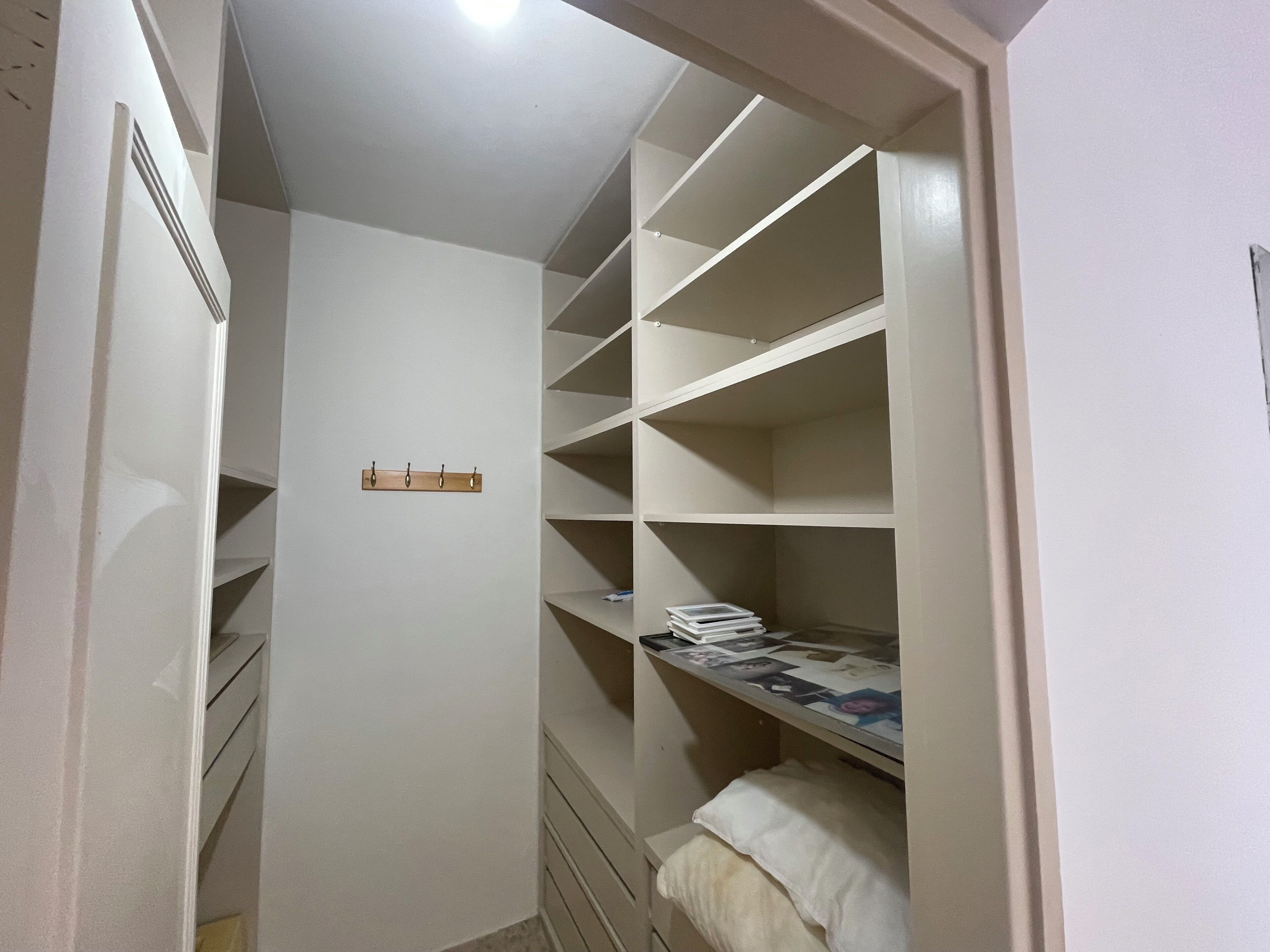 Un vestidor amplio con estantes varios y una cama con colchón blanco.