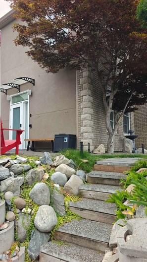 A stone staircase leading to a building with a stone facade, a red chair, and a tree with autumn leaves.