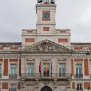 A historic building with a central clock tower, symmetrical windows, and a balcony with railings.