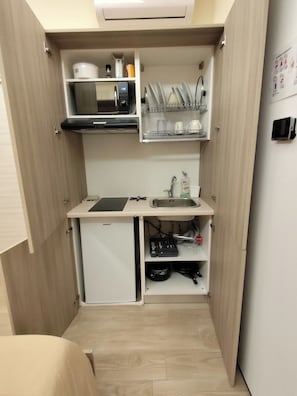 A compact kitchenette with a microwave, a small refrigerator, a sink, and a dish rack.