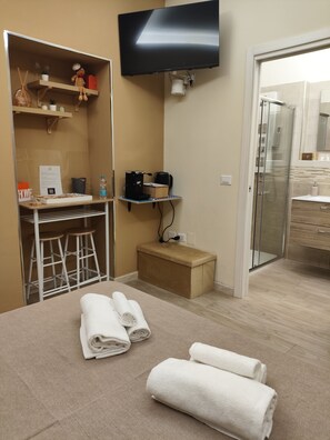 Une chambre d’hôtel comprenant un lit, un bureau avec un ordinateur, une télévision, une douche et un petit coin salon.