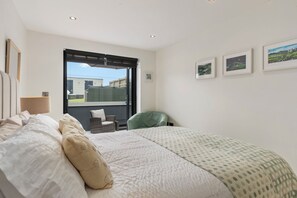 A bedroom with a large bed, a chair, a window, and artwork on the wall. - Monkstone View - Direct Beach Access (Saundersfoot)