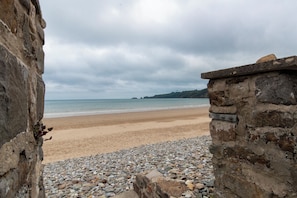 A beach with a stone wall and pebbles in the foreground, leading to a sandy shore and calm sea under cloudy skies. - Monkstone View - Direct Beach Access (Saundersfoot)