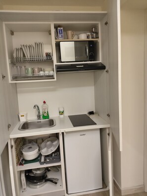Un angolo cottura compatto con microonde, piccolo frigorifero e lavello.