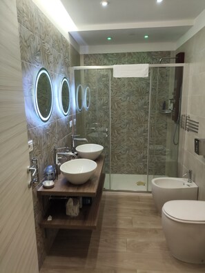 A modern bathroom with three sinks, a glass shower enclosure, and a toilet.