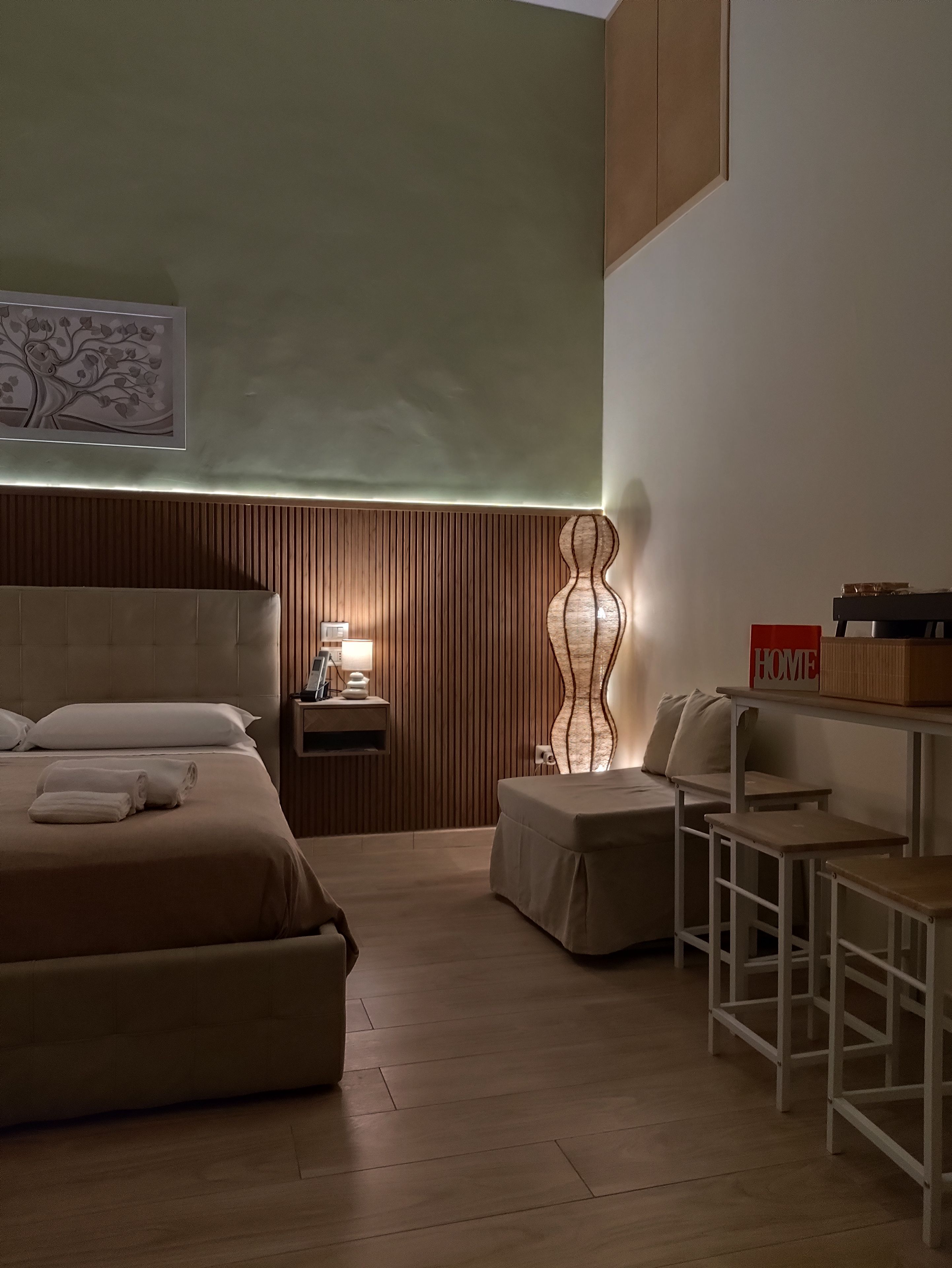 A hotel room with a bed, bedside table, lamp, and a decorative wall piece.