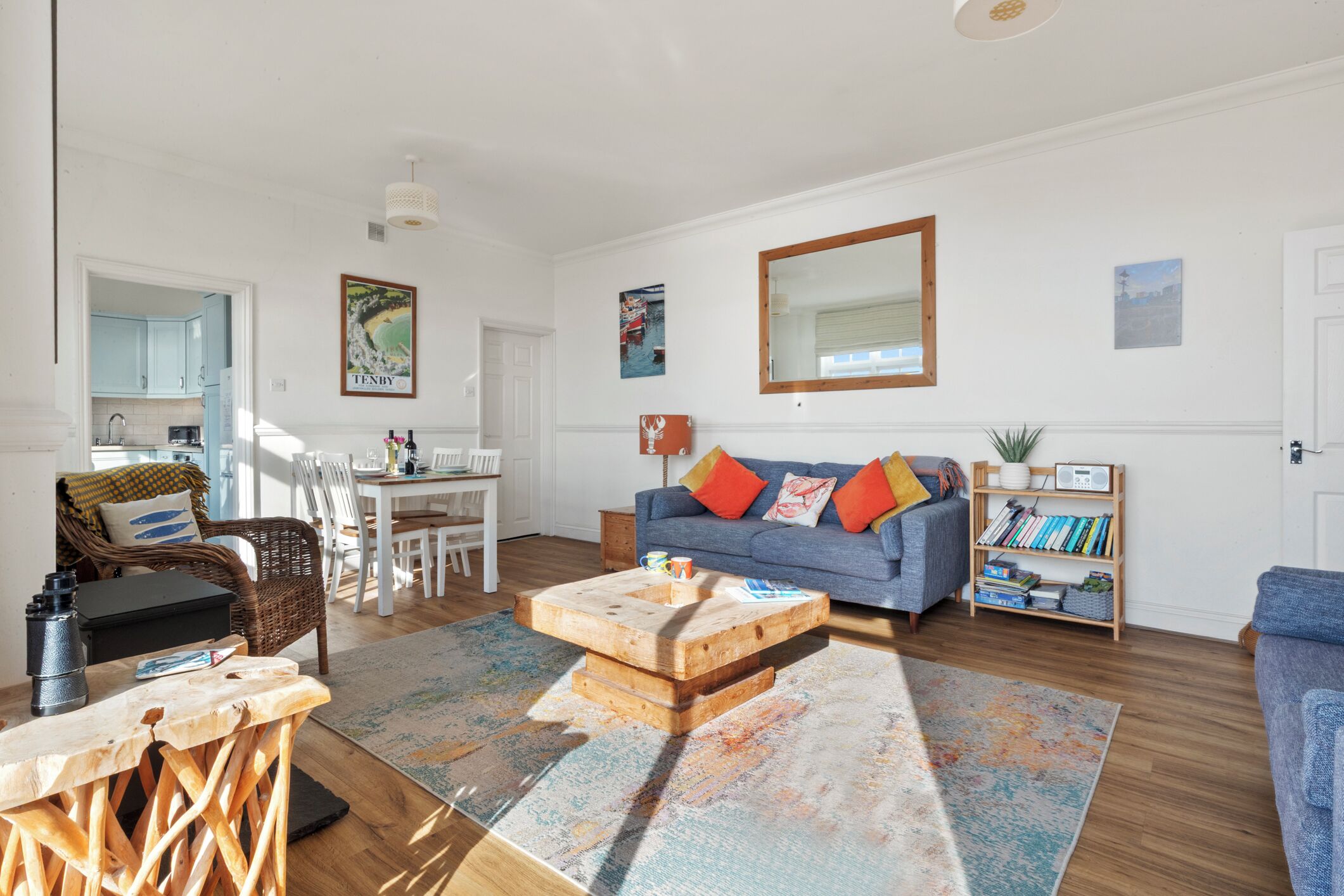 A spacious living room with a blue sofa, wooden coffee table, and a dining area with white chairs.