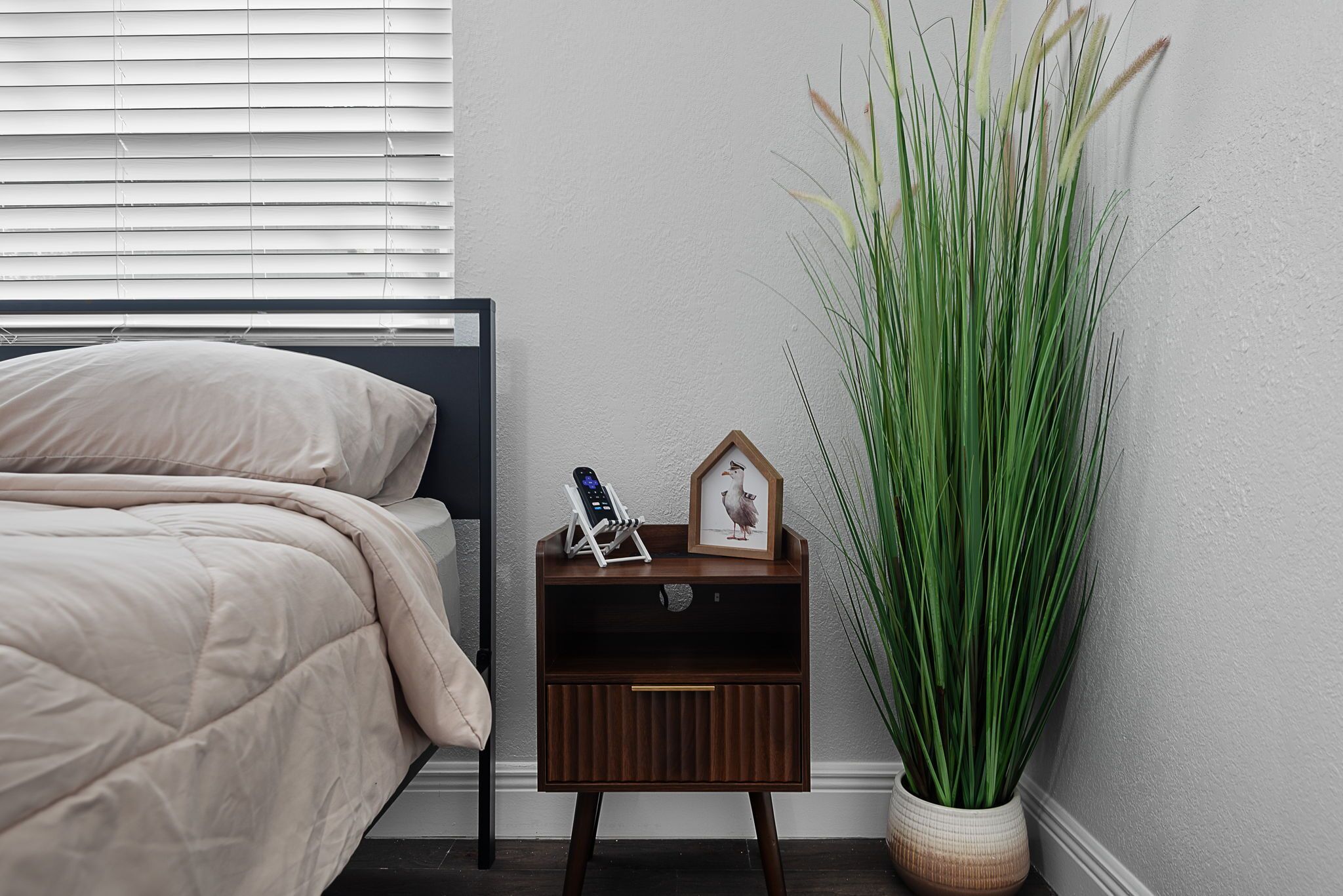 Een slaapkamer met een bed, nachtkastje en een hoge groene plant.