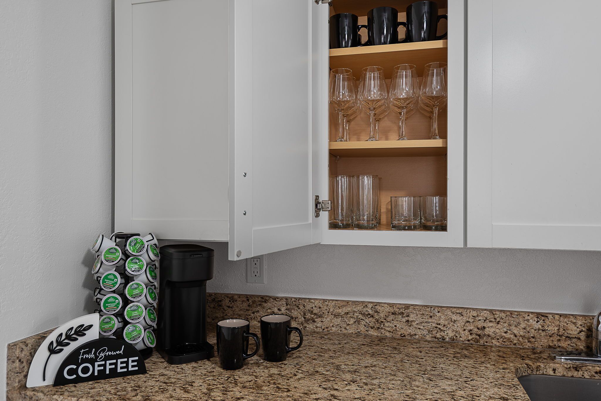 Een keuken met een koffieapparaat, mokken en een kast met glazen.