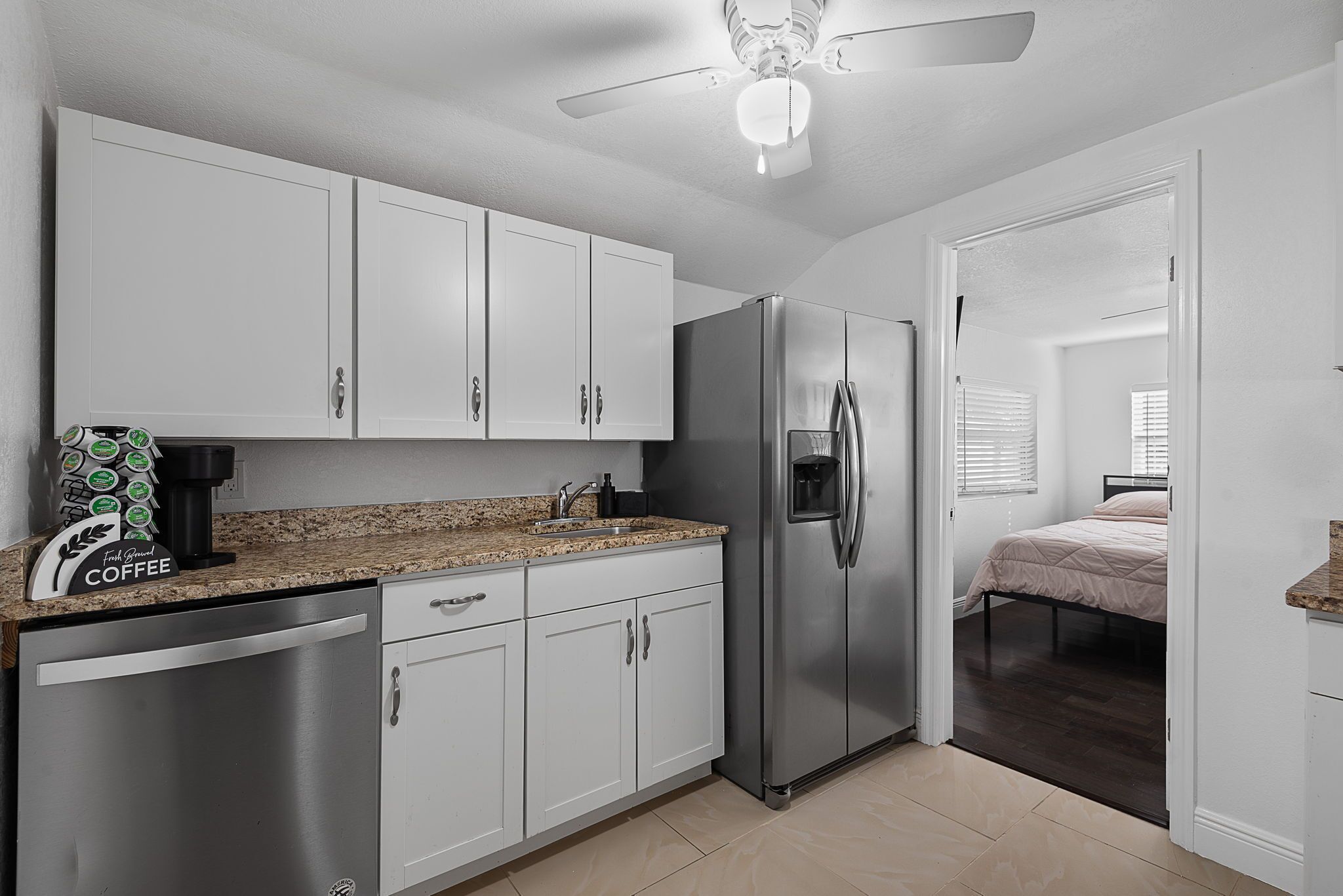 A compact kitchen with white cabinets, a stainless steel refrigerator, a coffee maker, and a ceiling fan.