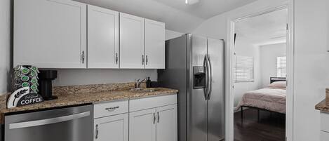 A compact kitchen with white cabinets, a stainless steel refrigerator, a coffee maker, and a ceiling fan.