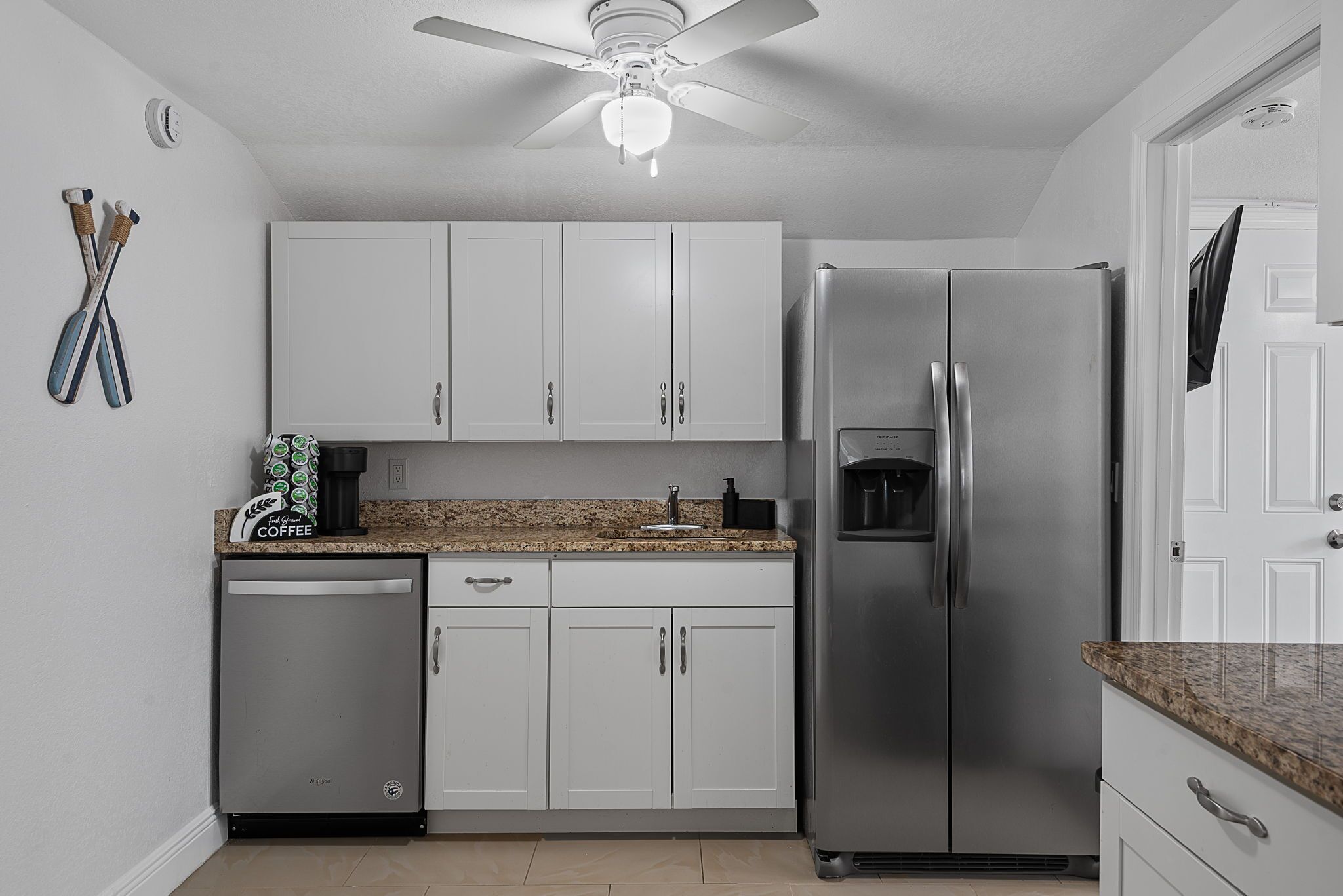 A kitchen with white cabinets, a stainless steel refrigerator, a dishwasher, and a coffee maker.