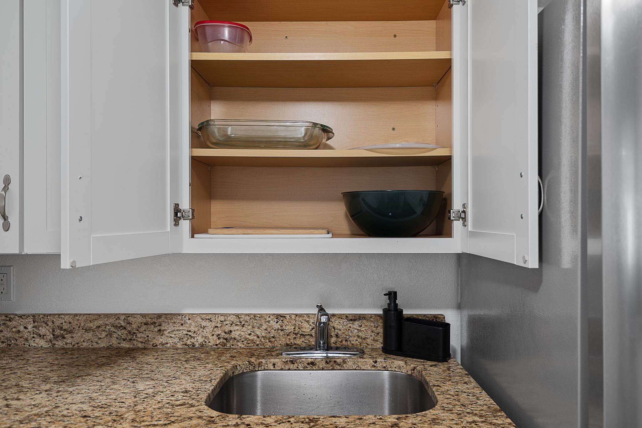 Una cucina con piano di lavoro in granito, lavello in acciaio inox e mobili in legno.