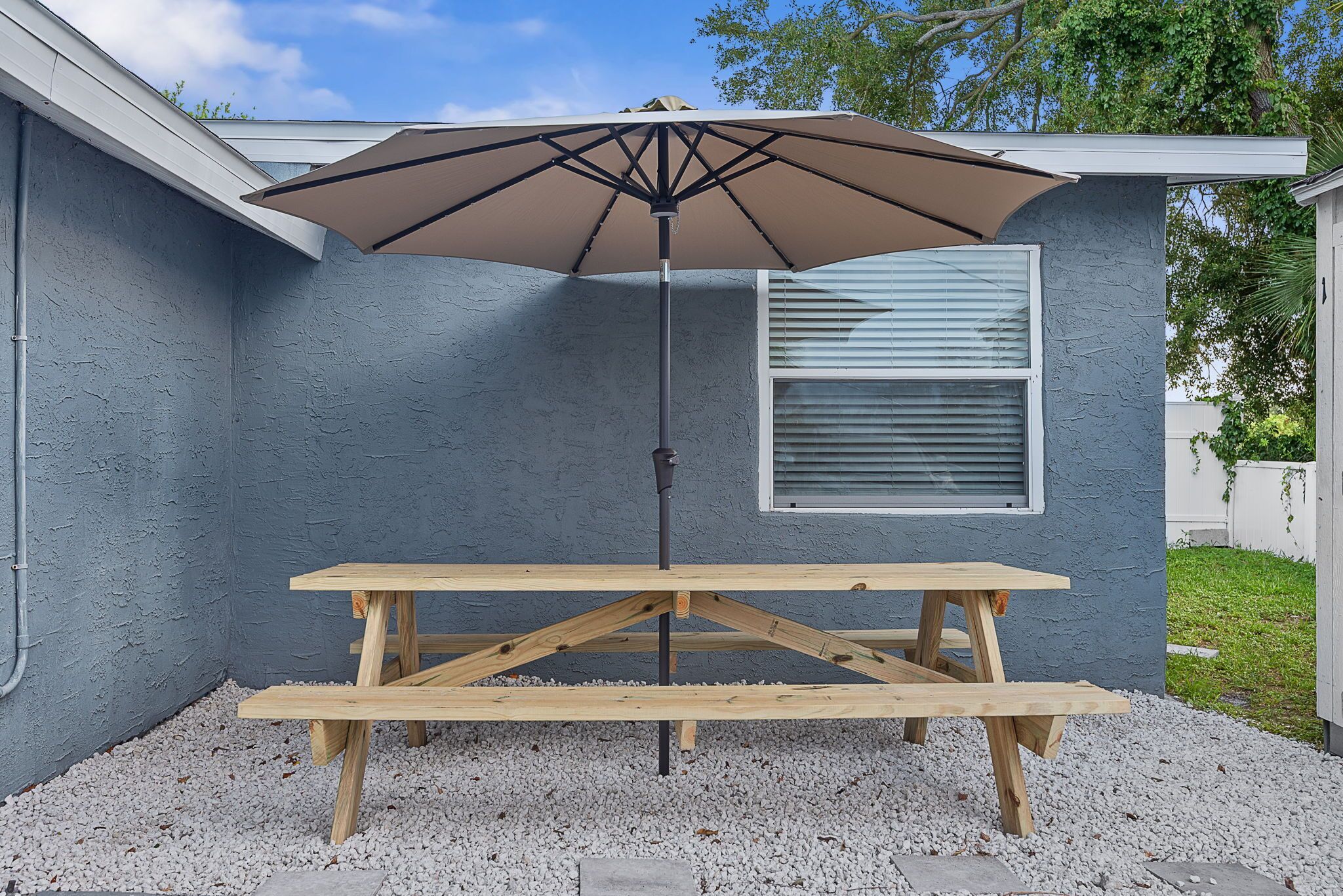 Een houten picknicktafel met een parasol voor een huis met een raam en een deur.