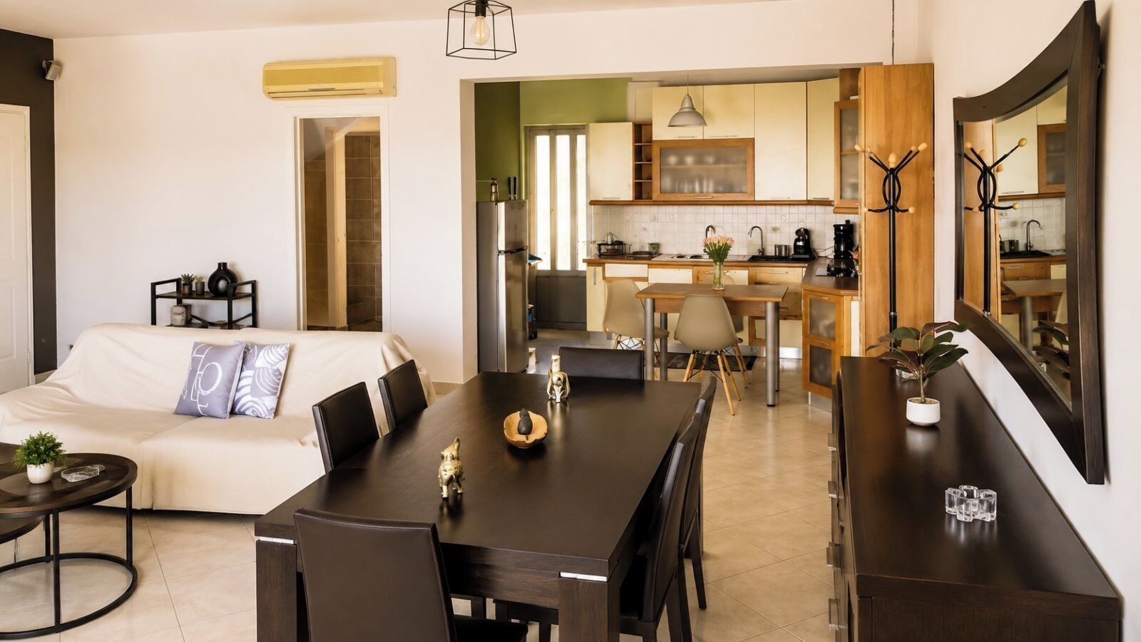 Un salon moderne avec un canapé, une table à manger et des chaises. On aperçoit une cuisine au fond.