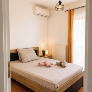 A neatly made bed with a headboard, an air conditioning unit mounted on the wall, a bedside lamp, and a window with curtains. - Καλώς ήρθατε στην υπέροχη μεζονέτα μας στο Κατάκολο! (Pirgos)