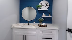 A bathroom with a white vanity, a round mirror, a 'Bath' sign, a small ship decoration, and a potted plant. - Beach Escape, Private Pool ,Sleeps 8 (Fort Myers Beach)