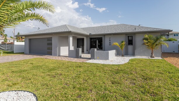 A modern single-story house with a grey roof, a front porch, and a small garden with palm trees. - Beach Escape, Private Pool ,Sleeps 8 (Fort Myers Beach)