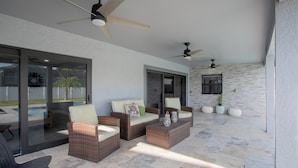 A covered patio area with wicker furniture, ceiling fans, and a stone wall. - Beach Escape, Private Pool ,Sleeps 8 (Fort Myers Beach)