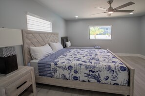 A bedroom with a bed, a nightstand, a ceiling fan, a window with a view, and a wall-mounted shelf. - Beach Escape, Private Pool ,Sleeps 8 (Fort Myers Beach)