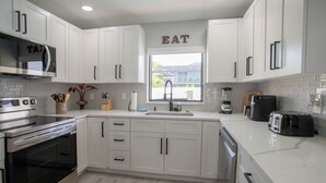 A modern kitchen with white cabinetry, a built-in oven, a stove, a sink, and a window with a view of the outside. - Beach Escape, Private Pool ,Sleeps 8 (Fort Myers Beach)