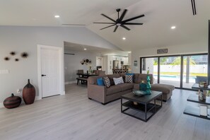 A modern living room with a sofa, coffee table, and decorative items. There is a dining area with a table and chairs visible in the background. - Beach Escape, Private Pool ,Sleeps 8 (Fort Myers Beach)