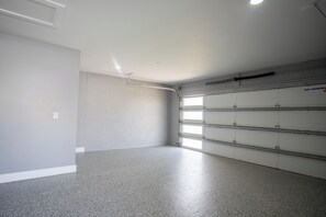 Un garage propre et dégagé, avec un sol en béton, des murs blancs et une porte de garage en métal dotée de plusieurs compartiments de rangement.