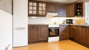 A kitchen with wooden cabinets, a white refrigerator, a stove, and a microwave. - Aurora House – A Family & Friends Retreat in Tromsø (Tromsø)