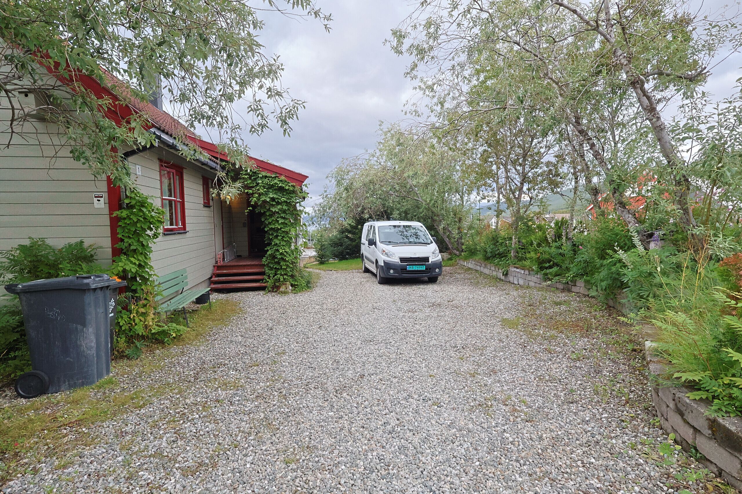 Een grindpad dat leidt naar een huis met een rood dak en een geparkeerde auto.