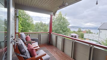 Ein überdachter Außenbereich mit Holzkästen und Kissen, mit Blick auf ein Gewässer und viel Grün.